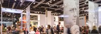 Besucher auf einer Messe, umgeben von modernem Standdesign und einem großen Porträt im Hintergrund.