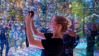 Frau fotografiert in einem mit Spiegeln und bunten Lichtern gestalteten Raum, ein Beispiel für immersive Erlebnisse auf Messen.